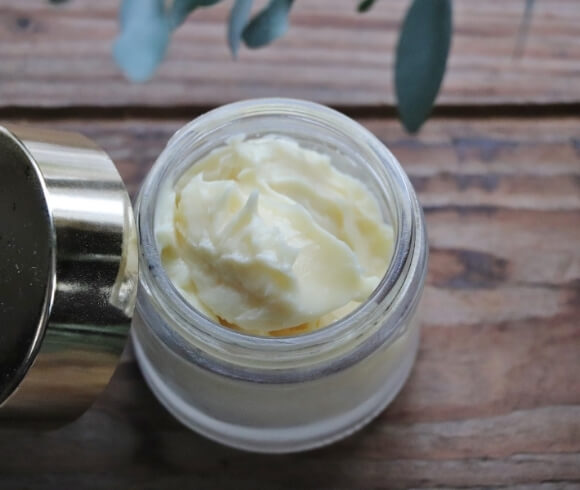 How To Make The Best Moisturizer For Dry Winter Skin image of jar of homemade moisturizer on wooden board with gold cover leaned up against the jar