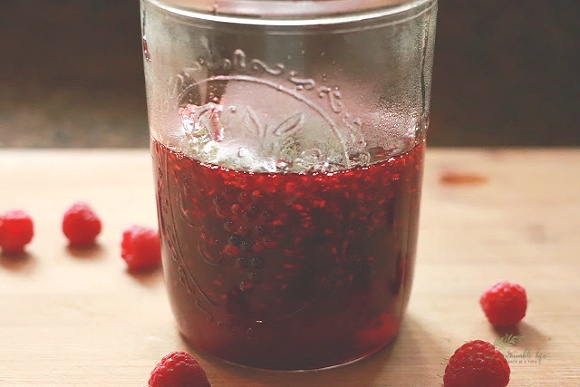 Red Raspberry Jam in mason jar on cutting board with a few fresh raspberrys on board
