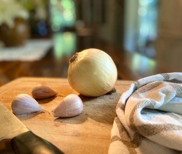 one pot thai beef curry recipe tutorial closeup image of onion and garlic cloves uncut resting on a cutting board with kitchen towel