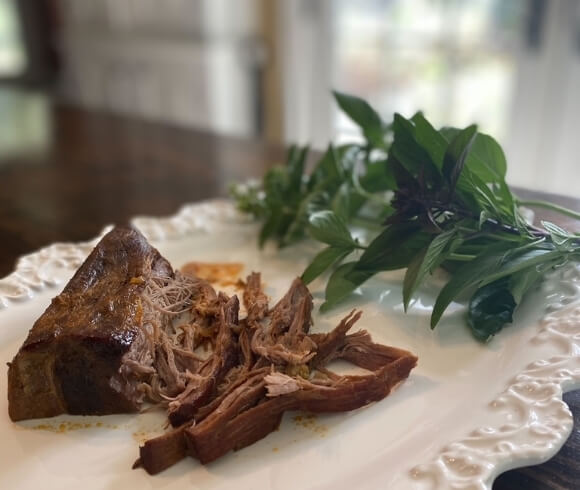 one pot thai beef recipe tutorial image displaying fresh basil sprigs resting on decorative white serving platter with tender cooked beef being shredded