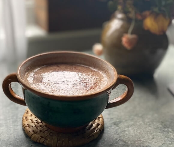 Easy Homemade Hot Chocolate Mix in pottery mug with two handles on rattan coaster with dried flowers in the background