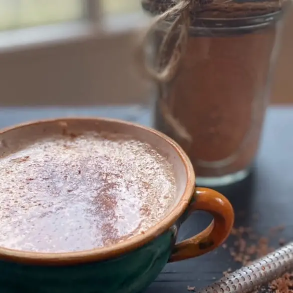 Easy Homemade Hot Chocolate Mix made into hot chocolate in mug with a mason jar container tied with twine filled with the hot chocolate mix in the background