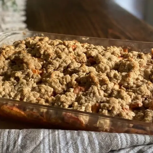 Homemade Gluten-Free Apple Crisp image of baked apple crisp in pan on wooden countertop with brown and white striped kitchen towel by the pan