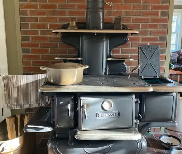 Heating With Wood image of antique Glenwood cookstove with pot on top, clothes drying, and water lid open