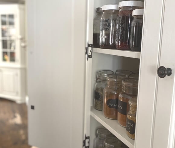 Home Apothecary Essential image showing herbs, spices, and remedies in jars on shelves in cupboard with door open