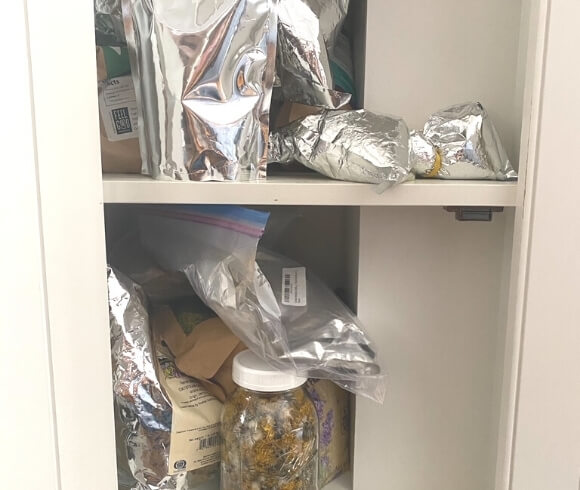 Home Apothecary Essentials image showing unorganized bags of herbs stuffed on shelves in cupboard
