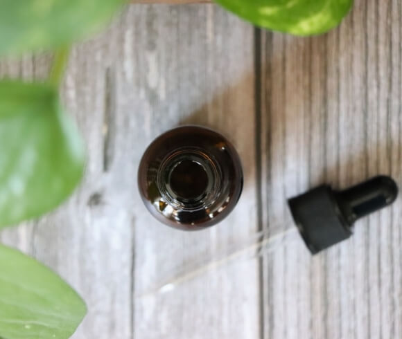 Herbal Tinctures {Folkoric & Measurement Method} image showing tincture bottle open looking down at in with greenery above and dropper laying beside the bottle