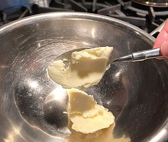 Healing DIY Gardener's Hand And Skin Salve image showing shea butter being dropped into stainless pan