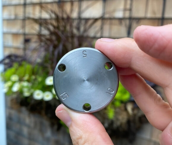 Canning Methods - Which To Use image showing closeup of pressure canning weight in front of blurred flower hanger