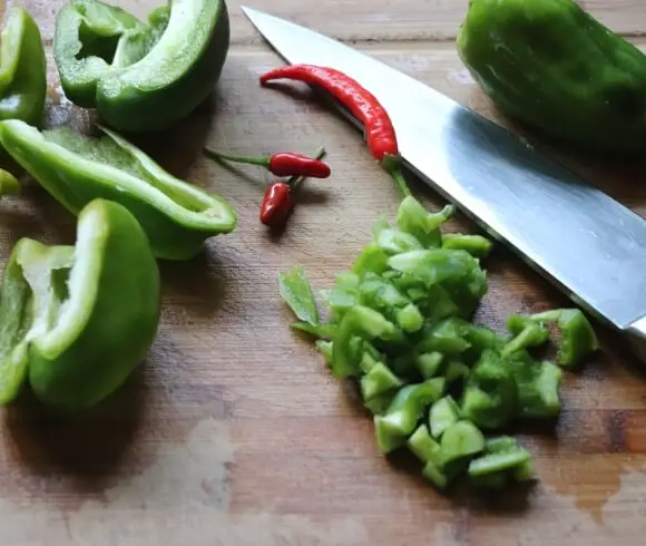 New England Style American Chop Suey image showing fresh green peppers that have been sliced 3 red hot peppers, and knife all resting on a cutting board