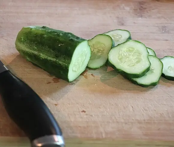 No Cook Refrigerator Pickles image showing fresh whole cucumber on cutting board with half of it sliced