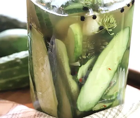 No Cook Refrigerator Pickles image showing closeup view of sliced cucumbers in a jar with vinegar brine and seasonings