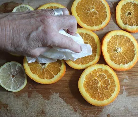 Making Dried Fruit Decorations image showing orange slices resting on wooden board with hand holding a paper towel to pat the slices dry
