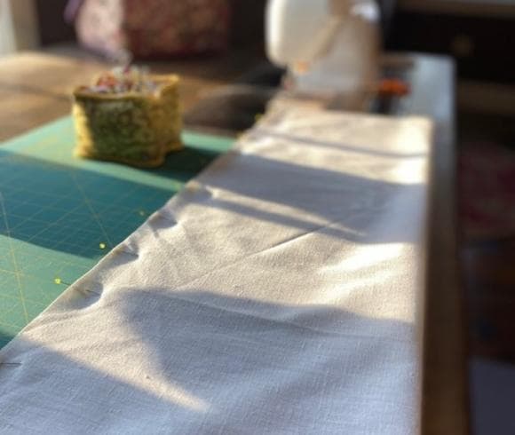 DIY Linen Bread Bag image showing length of white linen pinned on one side laying on green cutting mat with blurred background highlighting green square pin cushion