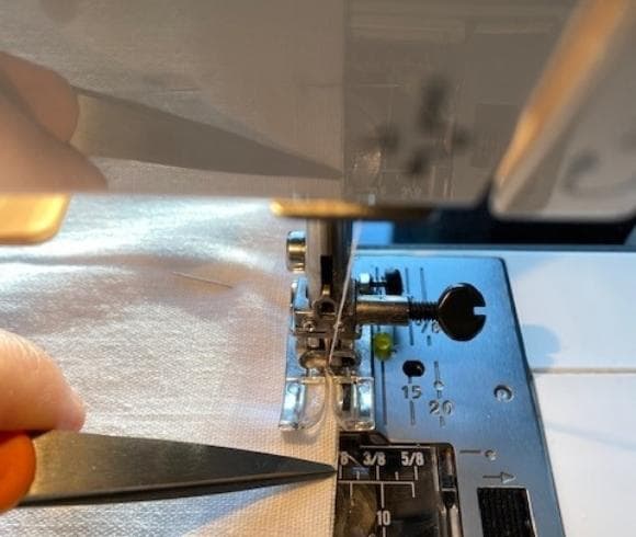 DIY Linen Bread Bag tutorial image showing white linen in sewing machine with scissor point showing the 1/8 inch mark on the sewing machine