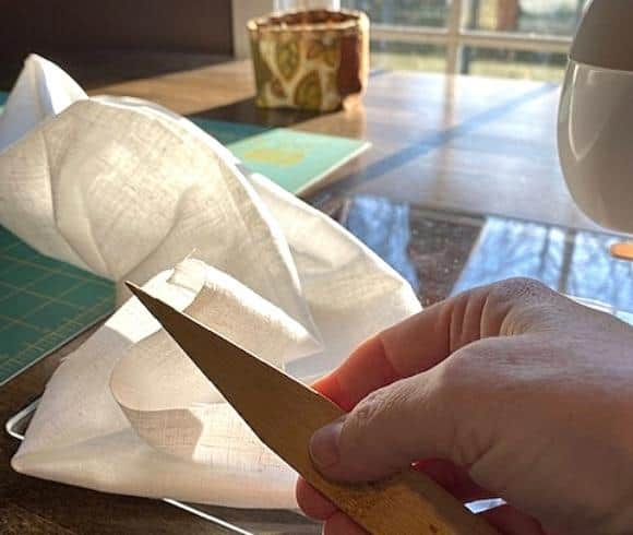 DIY Linen Bread Bag tutorial for how to make your own linen bread bag for homemade bread showing hand holding wooden point turner in front of blurred background showing sewing table and window with bright light coming in