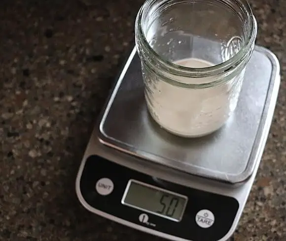 Reviving Refrigerated Sourdough Starter image. showing 50 grams of sourdough starter in mason jar resting on kitchen scale displaying 50 g indicator