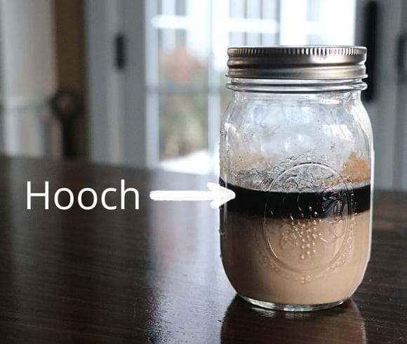 Reviving Refrigerated Sourdough Starter image showing mason jar with sourdough started just taken from the refrigerator with distinct separation of brown liquid "hooch" on top of lower level of tan colored sourdough paste (starter)