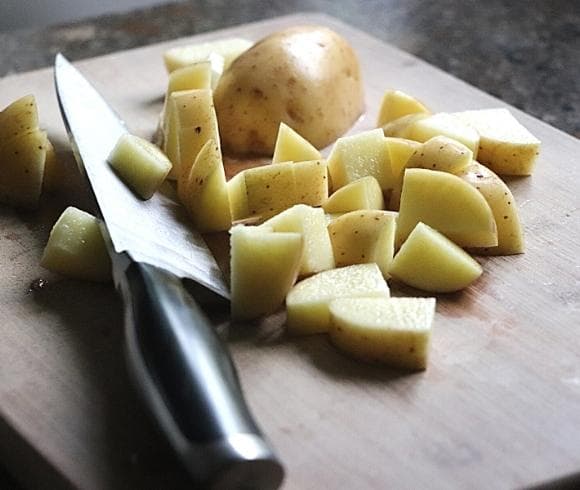 Old Fashioned Corn Chowder Recipe image showing knife with black handle resting on wooden cutting board with diced fresh potato pieces by the blade