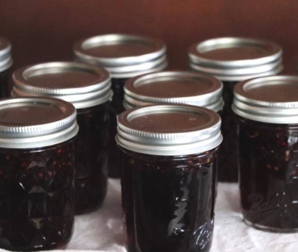 Elderberry Jam Recipe image showing 7 mason jars filled and sealed with elderberry jam resting on white surface
