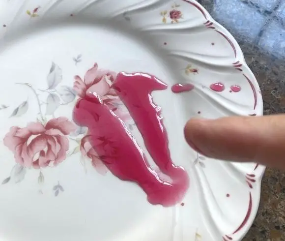 Elderberry Jam Recipe image showing jam gel test with liquid jam on a flowered plate showing space in the center of the jam where finger ran through the center of the jam