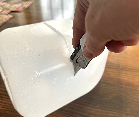 Winter Sowing In Milk Jugs image showing hand holding box cutter and cutting around the circumference of a milk jug