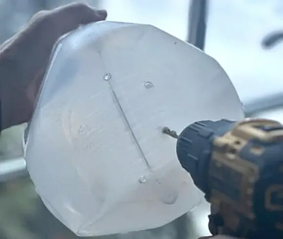 Winter Sowing In Milk Jugs image showing hand holding an empty milk jug with drill being used to poke holes in the bottom of the jug